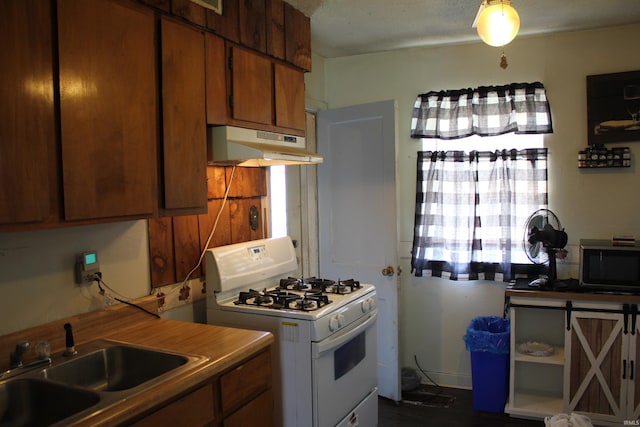2012 S Vine St, Muncie, IN 47302 - kitchen with white range with gas cooktop, under cabinet range hood, brown cabinetry, and stainless steel microwave