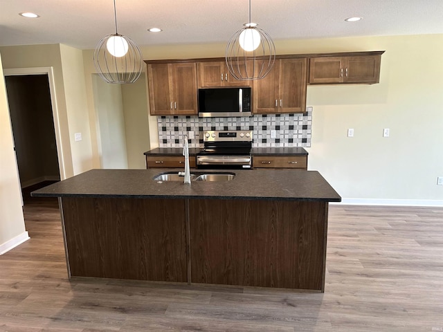 1466 Monte Carlo Dr, Huntertown, IN 46748 - kitchen featuring appliances with stainless steel finishes, tasteful backsplash, light wood-style flooring, hanging light fixtures, and an island with sink