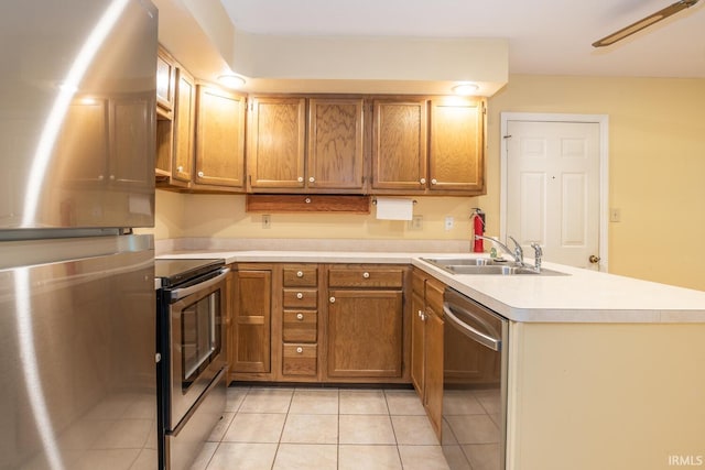 3718 Grasstree Ct, Bloomington, IN 47401 - kitchen with stainless steel appliances, a peninsula, light tile patterned flooring, light countertops, and brown cabinets