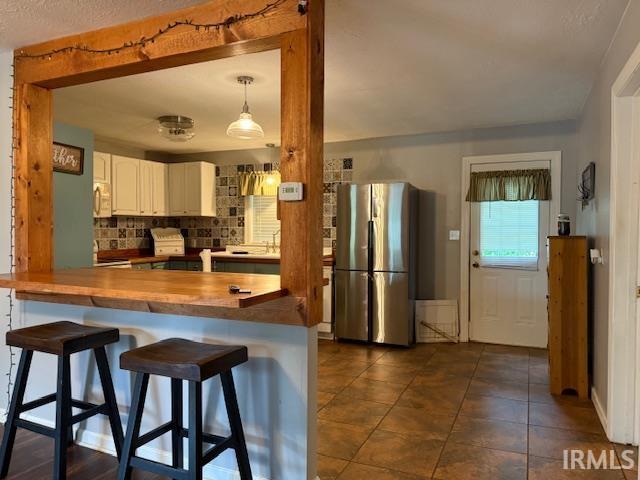 701 E Water St, Princeton, IN 47670 - kitchen featuring freestanding refrigerator, backsplash, white microwave, white cabinets, and a kitchen bar