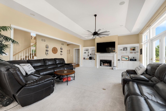 3631 E Pierceton Rd, Warsaw, IN 46580 - carpeted living room featuring a tray ceiling, built in shelves, a ceiling fan, a tile fireplace, and stairs