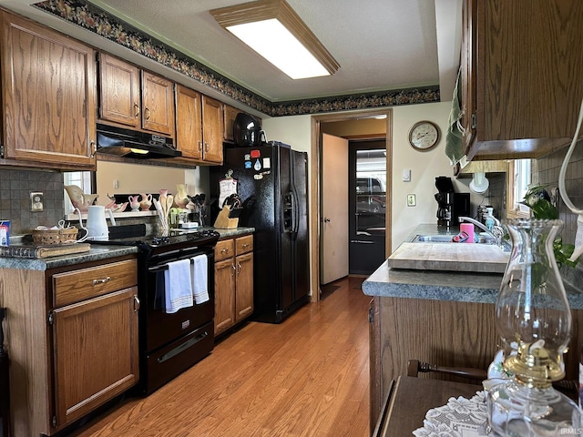 15908 Walnut St, Huntertown, IN 46748 - kitchen featuring under cabinet range hood, black appliances, backsplash, light wood-style floors, and brown cabinetry