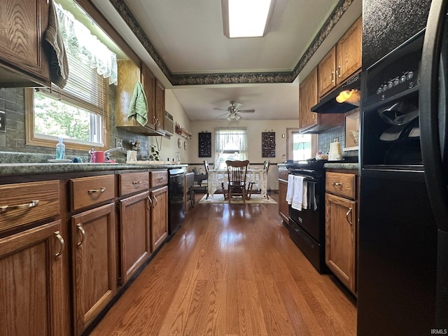15908 Walnut St, Huntertown, IN 46748 - kitchen featuring black appliances, wood finished floors, under cabinet range hood, brown cabinets, and dark countertops
