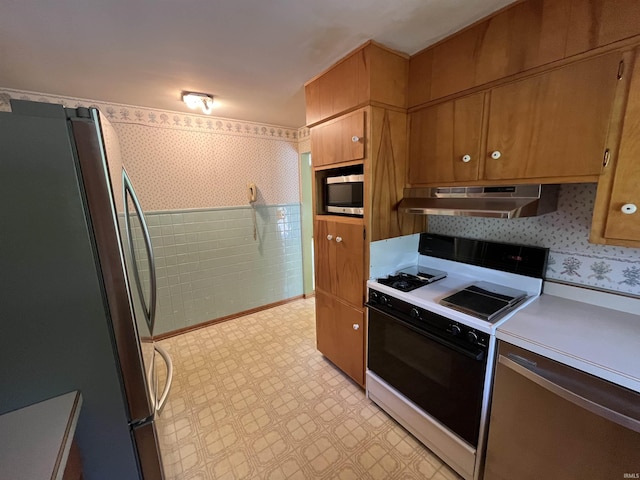 2127 Flora Dr, Peru, IN 46970 - kitchen with stainless steel appliances, under cabinet range hood, light countertops, light flooring, and wallpapered walls