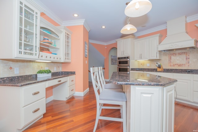 6488 Pebble Pointe Ct, Newburgh, IN 47630 - kitchen with premium range hood, stainless steel double oven, glass insert cabinets, light wood finished floors, and a breakfast bar