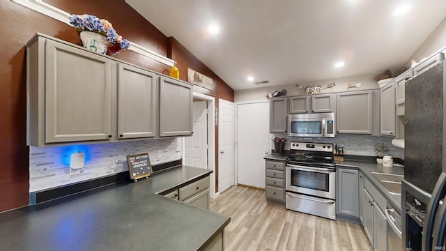 921 W Wheatfield Ln, Churubusco, IN 46723 - kitchen featuring stainless steel appliances, gray cabinetry, dark countertops, decorative backsplash, and lofted ceiling