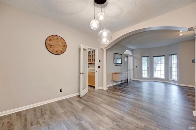1045 E Chris Ln, Bloomington, IN 47401 - spare room featuring arched walkways, light wood-type flooring, decorative columns, and a textured ceiling