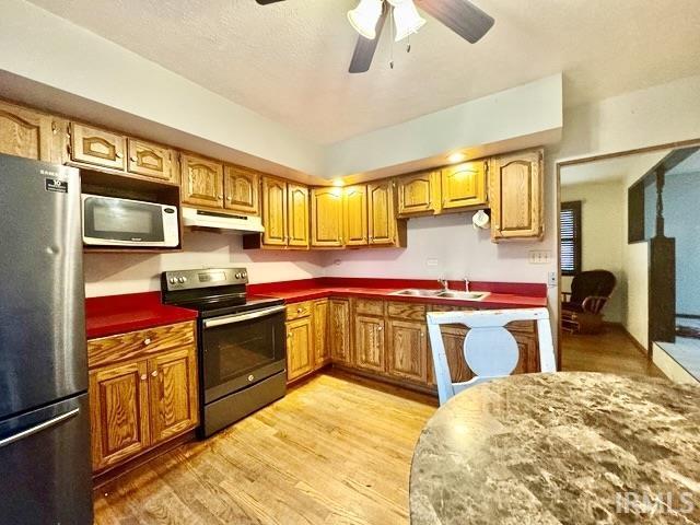 54213 Terrace Ln, South Bend, IN 46635 - kitchen featuring appliances with stainless steel finishes, under cabinet range hood, light wood-type flooring, ceiling fan, and brown cabinetry