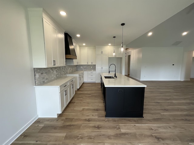 1609 Diane Dr, Ossian, IN 46777 - kitchen with wall chimney range hood, wood finished floors, backsplash, white cabinetry, and an island with sink