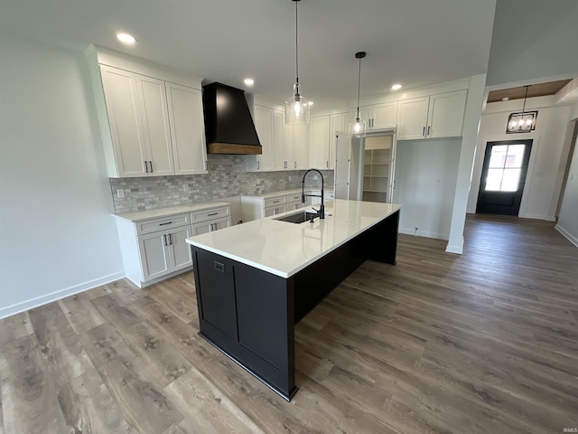 1609 Diane Dr, Ossian, IN 46777 - kitchen featuring custom exhaust hood, white cabinetry, decorative backsplash, an island with sink, and wood finished floors