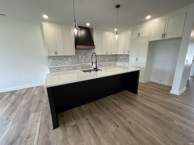 1609 Diane Dr, Ossian, IN 46777 - kitchen with wall chimney range hood, white cabinetry, wood finished floors, tasteful backsplash, and a center island with sink