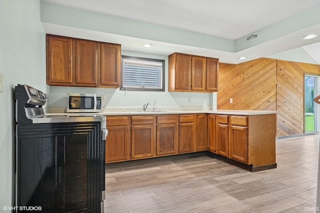19629 Gilmer St, South Bend, IN 46614 - kitchen featuring a peninsula, stainless steel microwave, brown cabinets, light wood finished floors, and light countertops