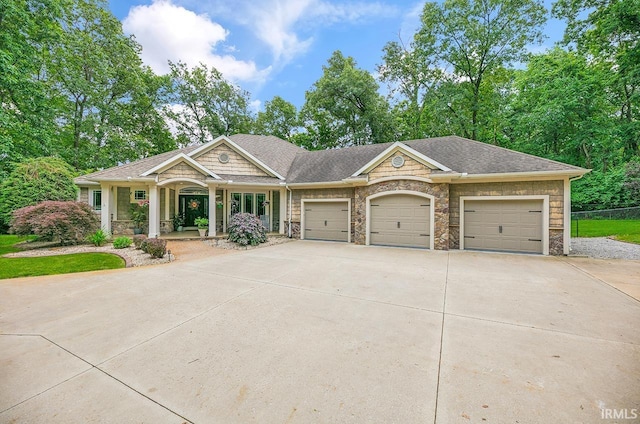 55623 Little Creek Ln, Middlebury, IN 46540 - view of front of house featuring stone siding, an attached garage, concrete driveway, a porch, and a shingled roof