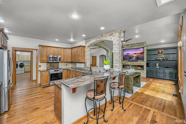 55623 Little Creek Ln, Middlebury, IN 46540 - kitchen with stainless steel appliances, washer and dryer, light wood-type flooring, a kitchen breakfast bar, and dark stone countertops