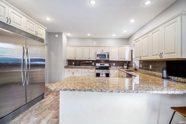 11999 Loughlin Dr, Mishawaka, IN 46545 - kitchen with appliances with stainless steel finishes, a peninsula, light wood-style flooring, light stone counters, and decorative backsplash