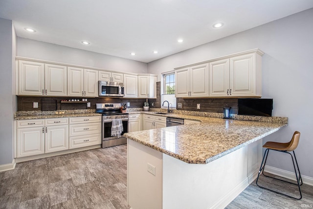 11999 Loughlin Dr, Mishawaka, IN 46545 - kitchen with stainless steel appliances, a peninsula, a breakfast bar area, light stone counters, and recessed lighting