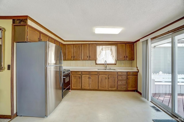 1049 Chapman Lake Dr, Warsaw, IN 46582 - kitchen featuring freestanding refrigerator, range with gas stovetop, brown cabinetry, a textured ceiling, and light countertops