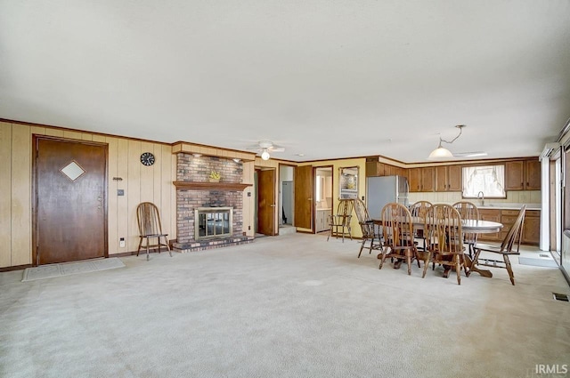 1049 Chapman Lake Dr, Warsaw, IN 46582 - dining area featuring a ceiling fan, a fireplace, wooden walls, light colored carpet, and ornamental molding