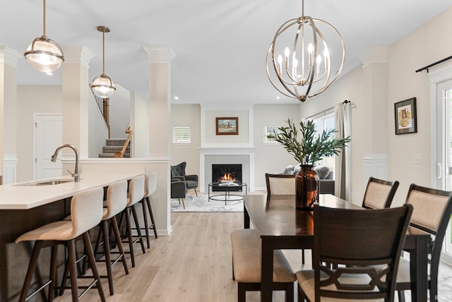 1114 Mosaic St, Huntertown, IN 46748 - dining room with light wood-style flooring, a warm lit fireplace, decorative columns, and stairs