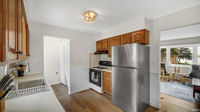 1897 Lakeshore Dr, Walkerton, IN 46574 - kitchen featuring freestanding refrigerator, white range with gas stovetop, wood finished floors, under cabinet range hood, and brown cabinetry