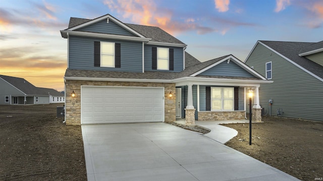 10263 Tirian Pl, Fort Wayne, IN 46835 - view of front of home featuring concrete driveway, stone siding, roof with shingles, an attached garage, and covered porch