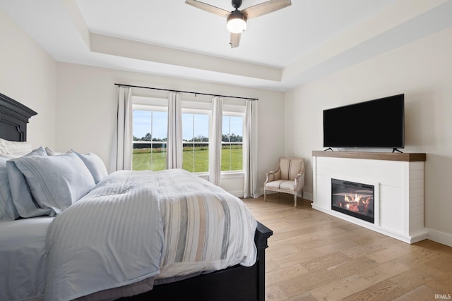 4685 N Triple Crown Dr, Bloomington, IN 47404 - bedroom with a tray ceiling, light wood-style floors, a glass covered fireplace, and a ceiling fan