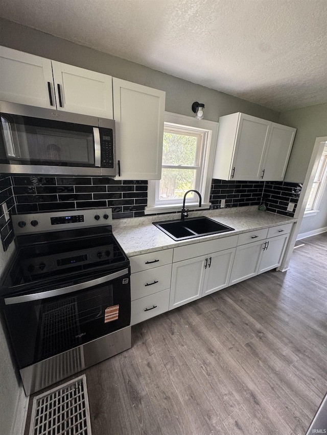 118 Burns Blvd, Fort Wayne, IN 46807 - kitchen with appliances with stainless steel finishes, a textured ceiling, white cabinetry, wood finished floors, and decorative backsplash
