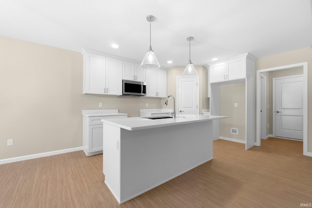 13969 Diavik Pl, Fort Wayne, IN 46845 - kitchen featuring stainless steel microwave, white cabinetry, light wood-style flooring, pendant lighting, and a center island with sink