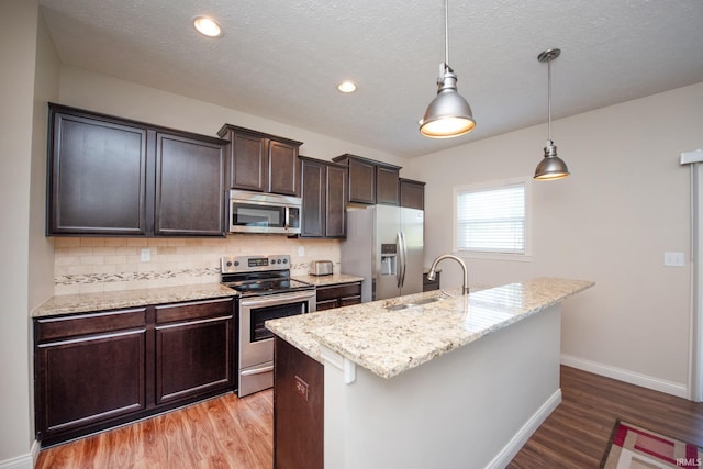 1860 Sandpiper Dr, West Lafayette, IN 47906 - kitchen featuring appliances with stainless steel finishes, light wood-style floors, backsplash, a center island with sink, and dark brown cabinets