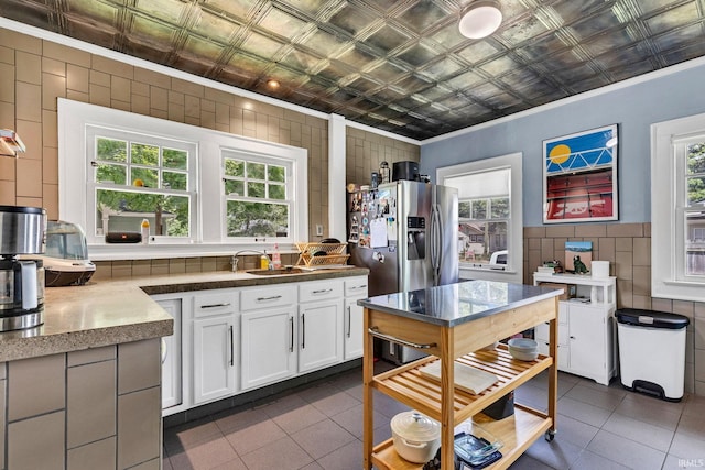 4721 Carrollton Ave, Indianapolis, IN 46205 - kitchen with an ornate ceiling, dark tile patterned floors, ornamental molding, white cabinetry, and stainless steel fridge with ice dispenser