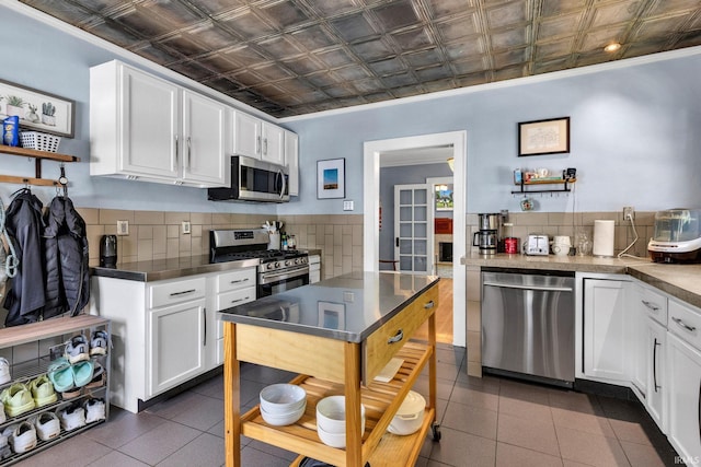 4721 Carrollton Ave, Indianapolis, IN 46205 - kitchen featuring appliances with stainless steel finishes, an ornate ceiling, white cabinets, backsplash, and dark tile patterned flooring