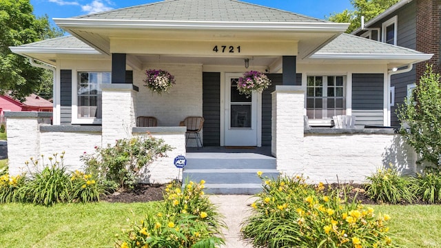 4721 Carrollton Ave, Indianapolis, IN 46205 - view of exterior entry with a porch, a shingled roof, and brick siding