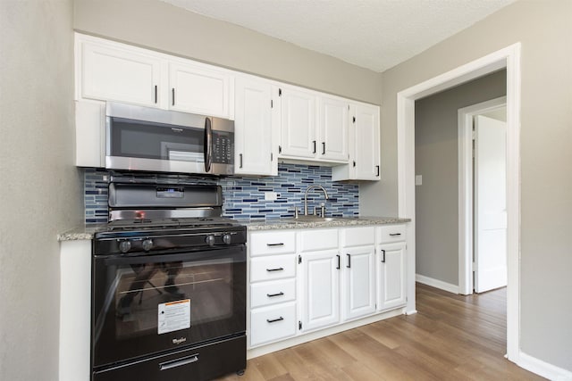 717 S Falcon St, South Bend, IN 46619 - kitchen featuring stainless steel microwave, gas stove, backsplash, light wood-style floors, and white cabinets