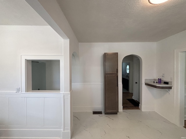 2521 N Red Bank Rd, Evansville, IN 47720 - unfurnished room featuring arched walkways, a wainscoted wall, light marble finish flooring, and a textured ceiling