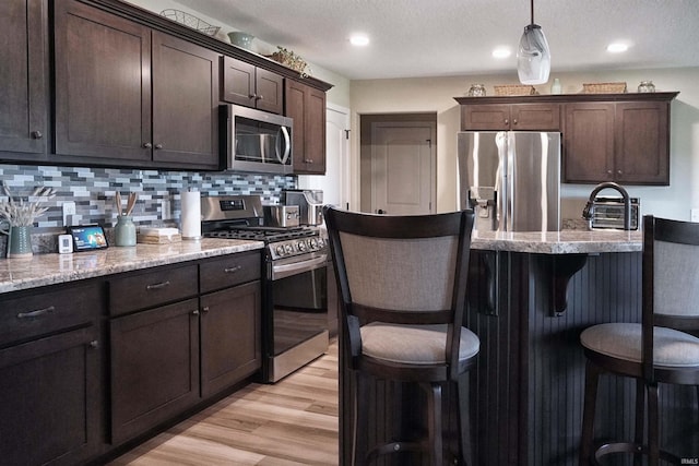 3065 E Butler Ct, Columbia City, IN 46725 - kitchen featuring appliances with stainless steel finishes, a breakfast bar, dark brown cabinets, decorative backsplash, and light wood-type flooring