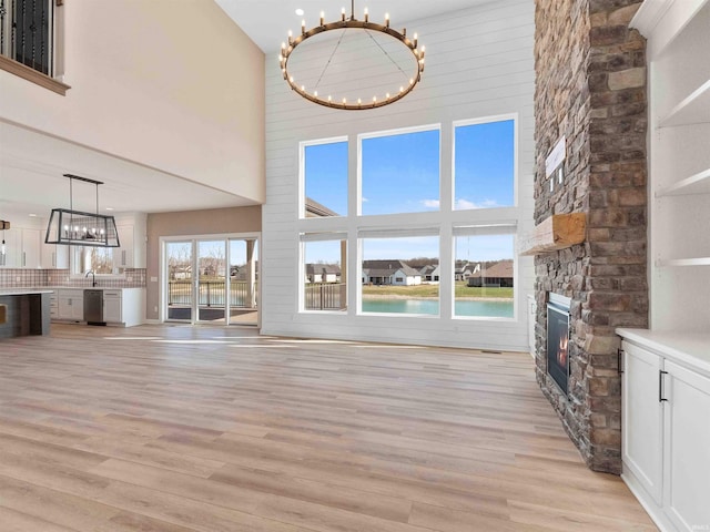 13092 Hallux Cv, Fort Wayne, IN 46845 - unfurnished living room with a chandelier, a stone fireplace, light wood finished floors, a towering ceiling, and a water view