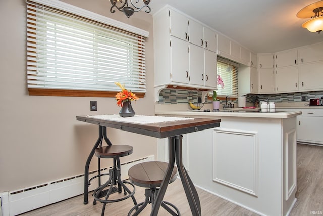 1401 S M St, Elwood, IN 46036 - kitchen featuring backsplash, light wood-style floors, light countertops, white cabinets, and a baseboard heating unit