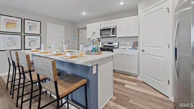 1185 Catesby Ct, Fort Wayne, IN 46818 - kitchen featuring stainless steel appliances, white cabinets, a kitchen island with sink, a kitchen bar, and light wood finished floors