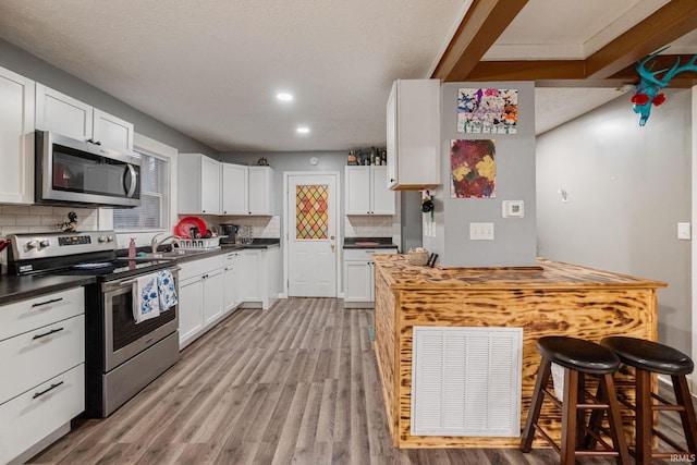 919 S 18th St, Lafayette, IN 47905 - kitchen featuring appliances with stainless steel finishes, tasteful backsplash, light wood-style flooring, a breakfast bar, and white cabinets