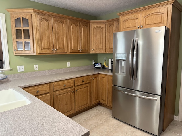 9825 Tamar Trl, Fort Wayne, IN 46825 - kitchen featuring stainless steel fridge, glass insert cabinets, light tile patterned floors, light countertops, and brown cabinets