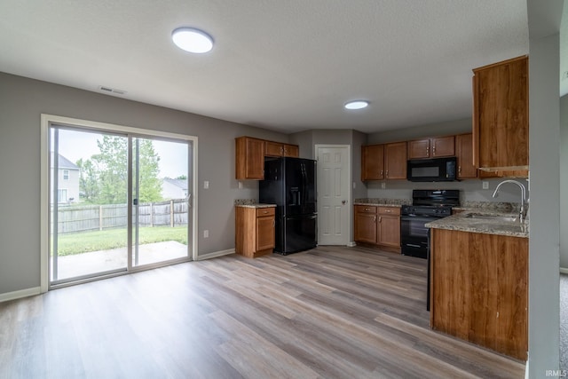 3827 Winter Raven Trl, Fort Wayne, IN 46818 - kitchen with black appliances, brown cabinetry, light wood finished floors, and light stone counters