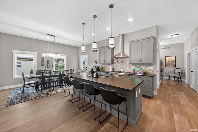 1229 Corby Blvd, South Bend, IN 46617 - kitchen with dark countertops, gray cabinets, wall chimney exhaust hood, a center island with sink, and light wood-style flooring