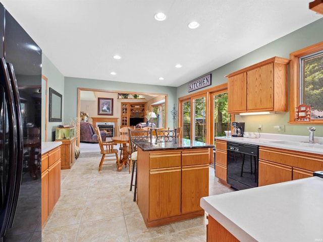 6709 Shag Bark Ct, Fort Wayne, IN 46835 - kitchen with black appliances, a center island, a glass covered fireplace, recessed lighting, and light tile patterned floors