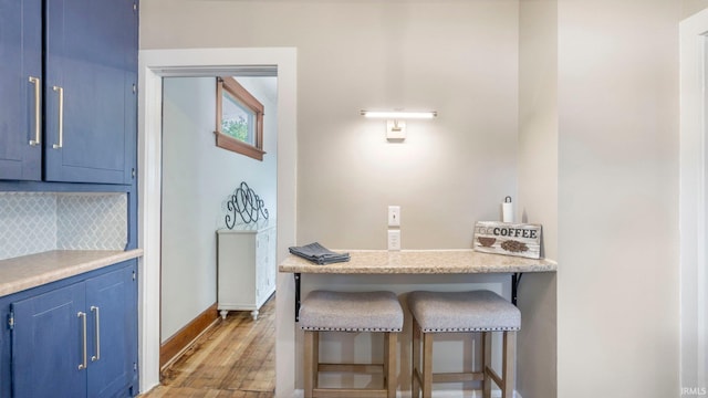 1607 Franklin Ave, Fort Wayne, IN 46808 - kitchen with blue cabinetry, tasteful backsplash, light wood-type flooring, a kitchen bar, and light countertops