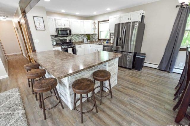 7132 W 350 N, West Lafayette, IN 47906 - kitchen with appliances with stainless steel finishes, white cabinets, decorative backsplash, light wood-style flooring, and a breakfast bar