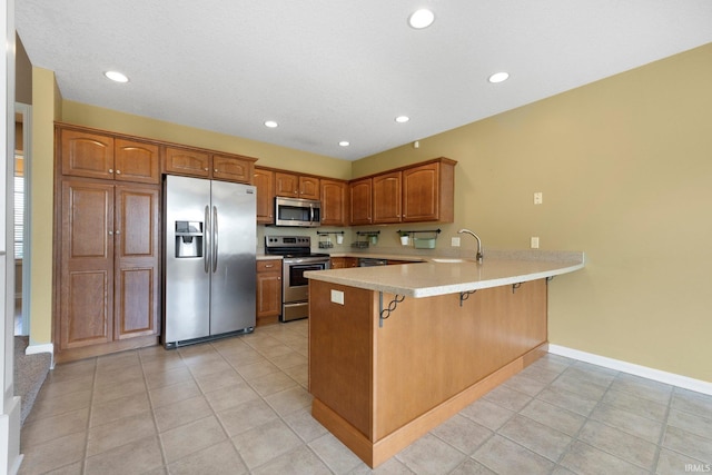 12828 Palazzo Blvd, Fort Wayne, IN 46845 - kitchen with stainless steel appliances, a peninsula, light countertops, a breakfast bar, and brown cabinets