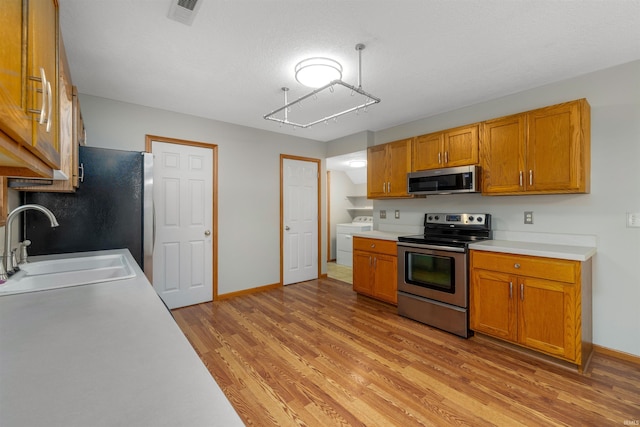 12531 Stoneboro Ct, Fort Wayne, IN 46845 - kitchen featuring appliances with stainless steel finishes, washer / dryer, light wood-style floors, brown cabinetry, and light countertops