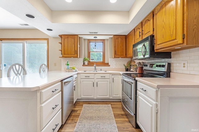 9026 Wallen Ln, Fort Wayne, IN 46825 - kitchen featuring stainless steel appliances, a peninsula, light countertops, light wood-type flooring, and tasteful backsplash