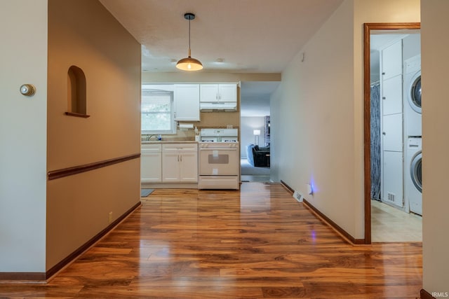1712 Royal Center Pike, Logansport, IN 46947 - kitchen featuring white gas range oven, stacked washer / dryer, under cabinet range hood, white cabinets, and wood finished floors