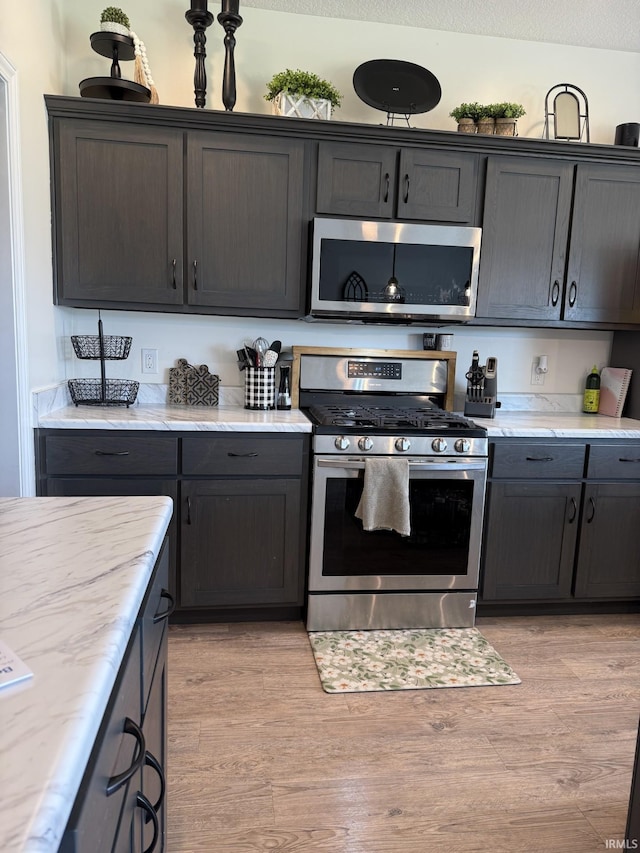 12788 Kingfish Ct, Middlebury, IN 46540 - kitchen featuring appliances with stainless steel finishes, light wood-style flooring, and light stone countertops